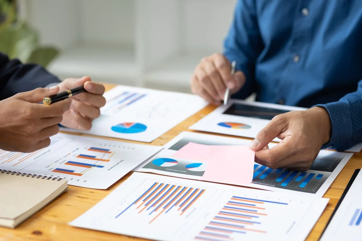 A close-up image of a meeting. Three people are visible looking over paper reports together.