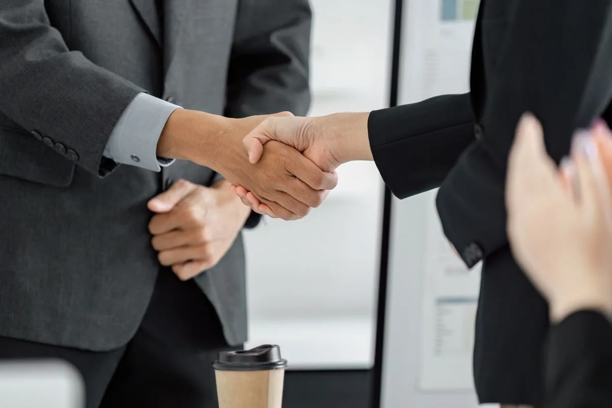A close-up image of a handshake between an employee and a client in a bright, modern office space.