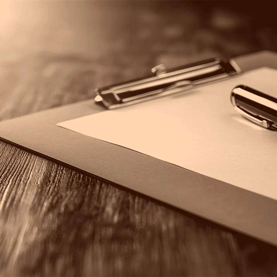 A close-up of a clipboard and a blank sheet of paper. A pen is resting on top of it.
