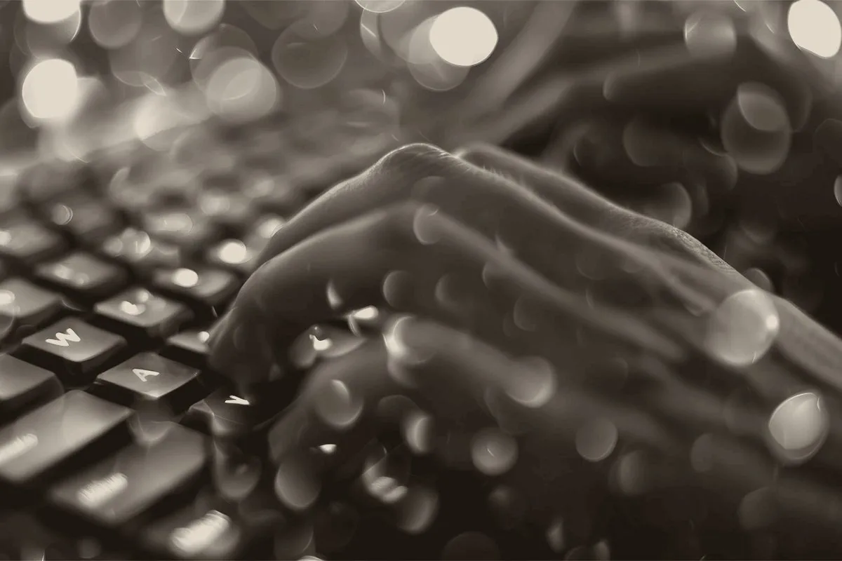 A close-up black and white image of a hand typing on a keyboard.